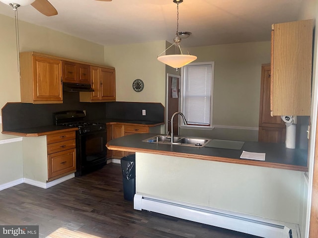 kitchen featuring black gas range, under cabinet range hood, a sink, dark countertops, and a baseboard radiator