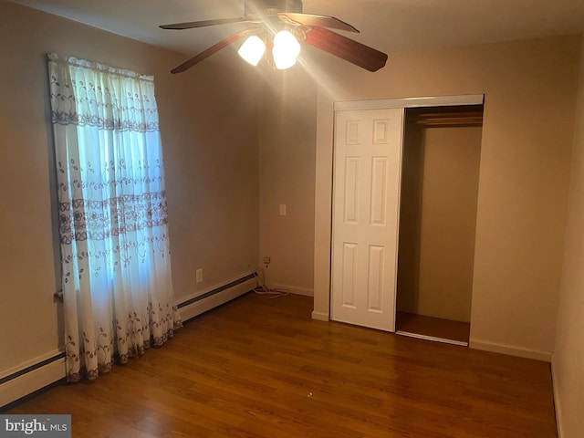 unfurnished bedroom featuring a baseboard heating unit, wood finished floors, a closet, and ceiling fan