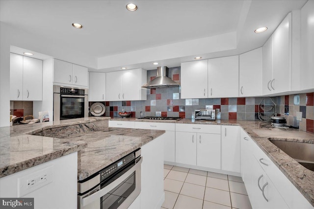 kitchen featuring backsplash, light tile patterned floors, white cabinets, stainless steel appliances, and wall chimney exhaust hood