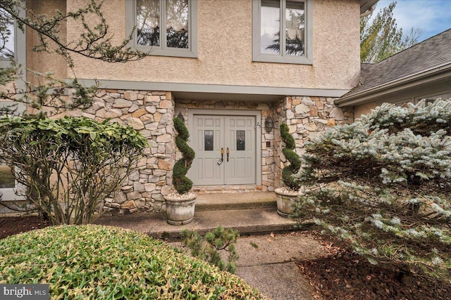 property entrance featuring stucco siding, stone siding, and roof with shingles