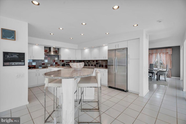 kitchen with light tile patterned floors, a breakfast bar area, freestanding refrigerator, and wall chimney range hood