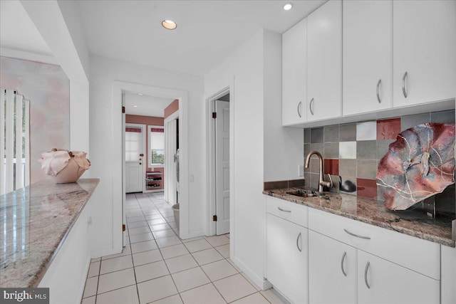 kitchen with light tile patterned floors, light stone countertops, a sink, white cabinetry, and tasteful backsplash