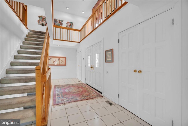 entrance foyer with stairway, light tile patterned floors, visible vents, and a high ceiling