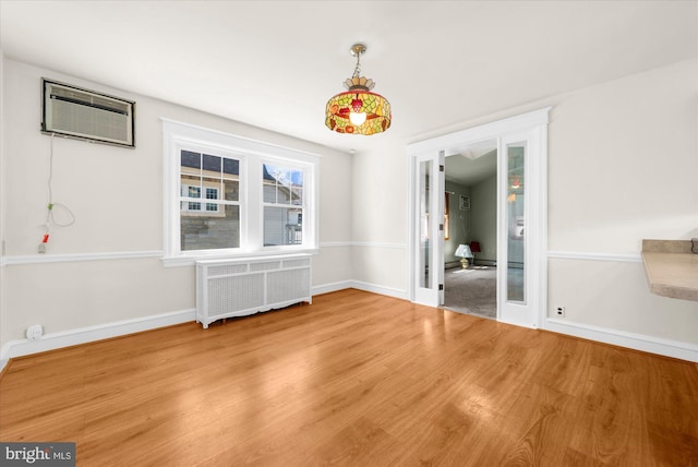 unfurnished dining area featuring radiator, a wall mounted air conditioner, baseboards, and wood finished floors