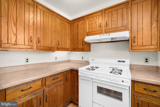 kitchen with light countertops, gas range gas stove, brown cabinetry, and under cabinet range hood