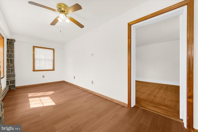 empty room with ceiling fan, a baseboard heating unit, baseboards, and wood finished floors