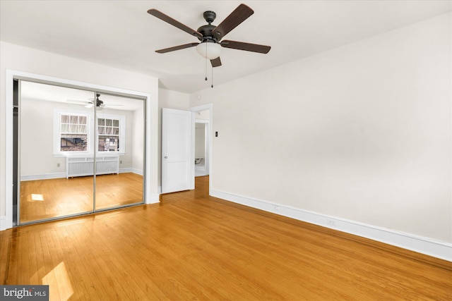 unfurnished bedroom featuring radiator, baseboards, ceiling fan, a closet, and wood-type flooring