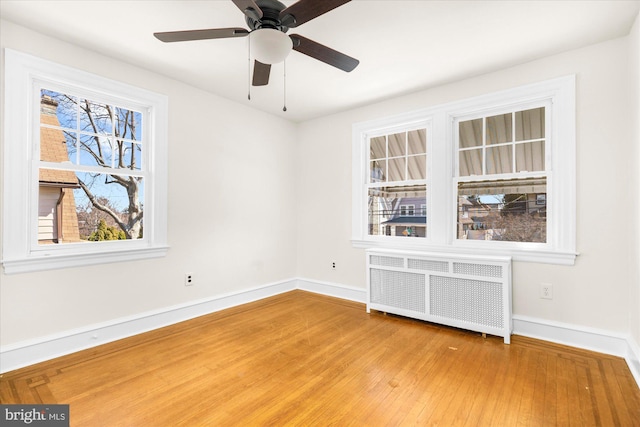 empty room featuring ceiling fan, radiator heating unit, baseboards, and wood finished floors