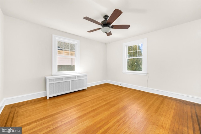 empty room with radiator, wood finished floors, baseboards, and ceiling fan