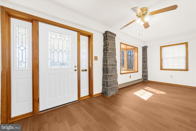 foyer featuring a baseboard heating unit, baseboards, ceiling fan, decorative columns, and wood finished floors