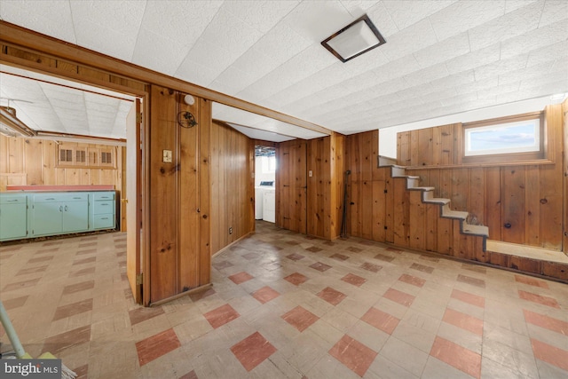 below grade area featuring stairs, washer / dryer, light floors, and wood walls