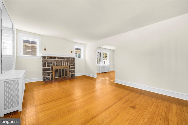 unfurnished living room with visible vents, wood-type flooring, arched walkways, a stone fireplace, and baseboards