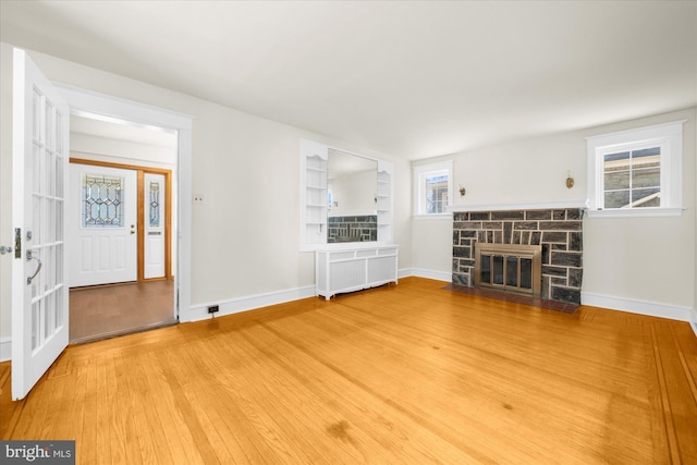 unfurnished living room featuring radiator heating unit, a fireplace, baseboards, and light wood finished floors