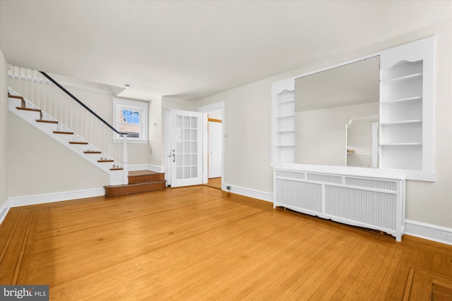 interior space featuring hardwood / wood-style floors, built in shelves, baseboards, radiator heating unit, and stairs