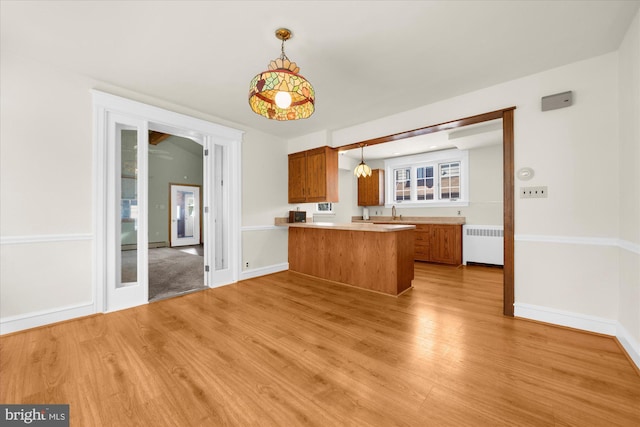 kitchen featuring a peninsula, radiator heating unit, brown cabinetry, and light wood finished floors