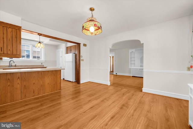 kitchen with radiator, brown cabinetry, freestanding refrigerator, light wood-style floors, and arched walkways