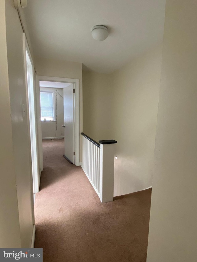 hall featuring an upstairs landing, baseboards, and carpet floors