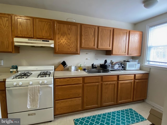 kitchen with white appliances, light countertops, under cabinet range hood, and a sink