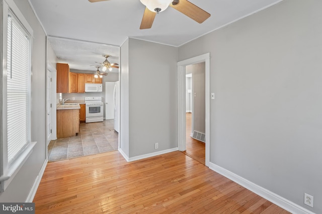 unfurnished living room featuring a sink, light wood-type flooring, baseboards, and visible vents