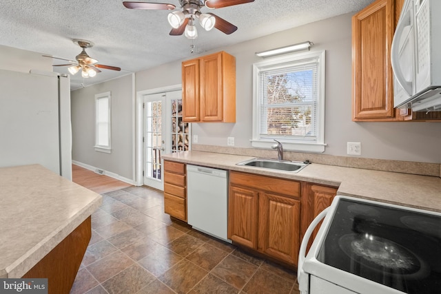 kitchen with baseboards, light countertops, white appliances, a textured ceiling, and a sink