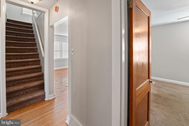 hall featuring light wood finished floors, a textured ceiling, stairs, and baseboards