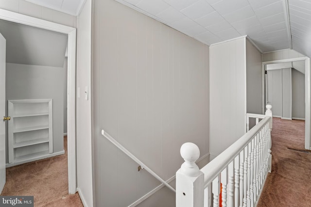 hallway with an upstairs landing, lofted ceiling, carpet floors, and crown molding