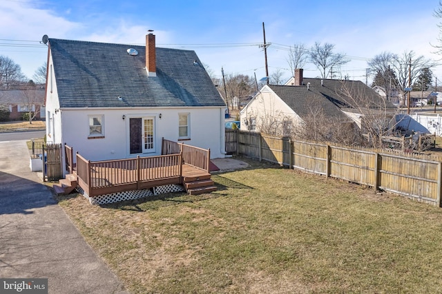 back of house featuring stucco siding, fence, a yard, a wooden deck, and a chimney