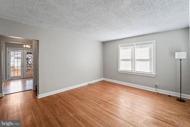 spare room featuring french doors, baseboards, a textured ceiling, and wood finished floors