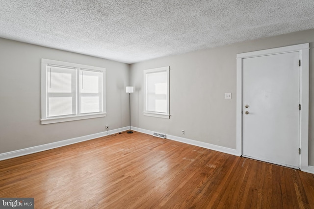 empty room featuring visible vents, a textured ceiling, baseboards, and wood finished floors