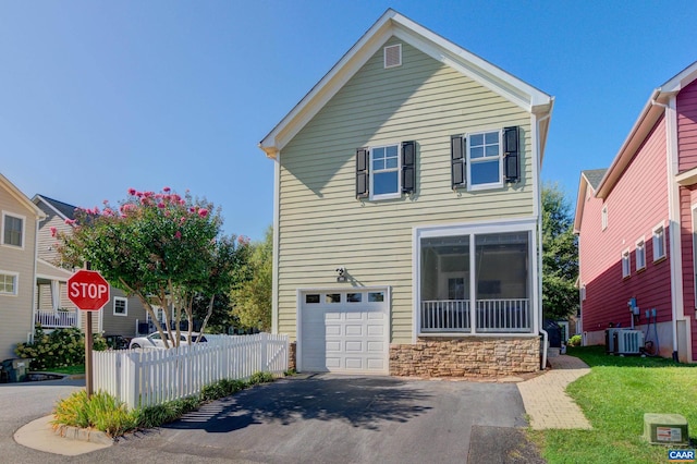 traditional-style home with fence, driveway, central AC, a garage, and stone siding