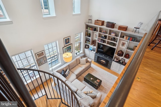 living room with stairs, wood finished floors, a towering ceiling, and a lit fireplace