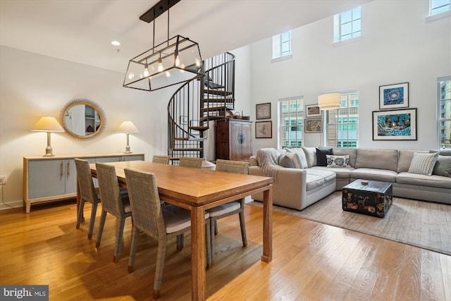 dining space with stairs, recessed lighting, light wood-style floors, a towering ceiling, and a notable chandelier