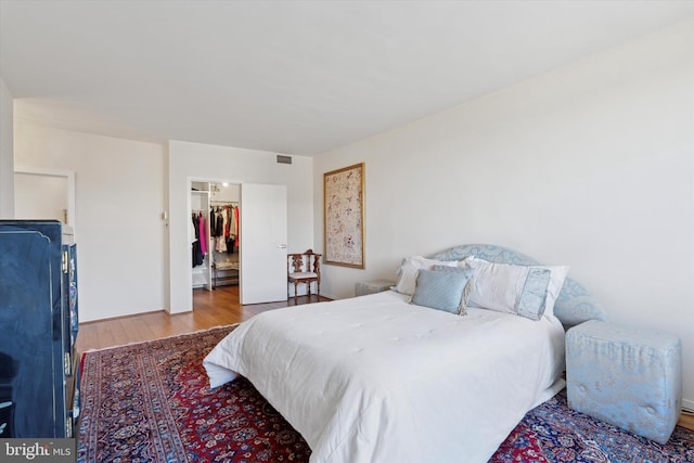 bedroom with a spacious closet, wood finished floors, visible vents, and a closet