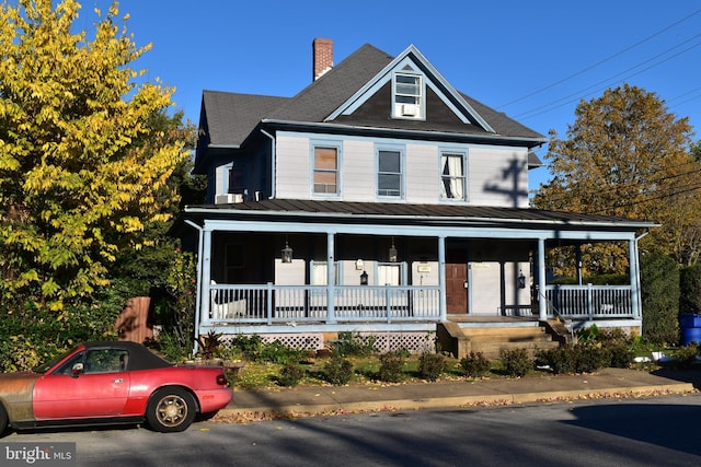 view of front facade featuring a porch, a chimney, and metal roof