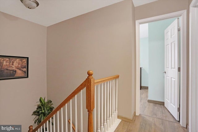 hall featuring baseboards, an upstairs landing, and light wood-style flooring