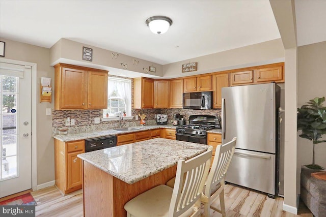 kitchen featuring light stone counters, decorative backsplash, plenty of natural light, black appliances, and a sink