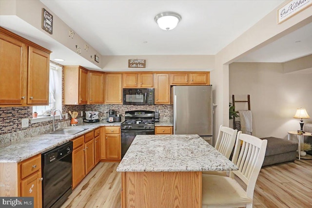 kitchen with a center island, decorative backsplash, light wood-style floors, black appliances, and a sink