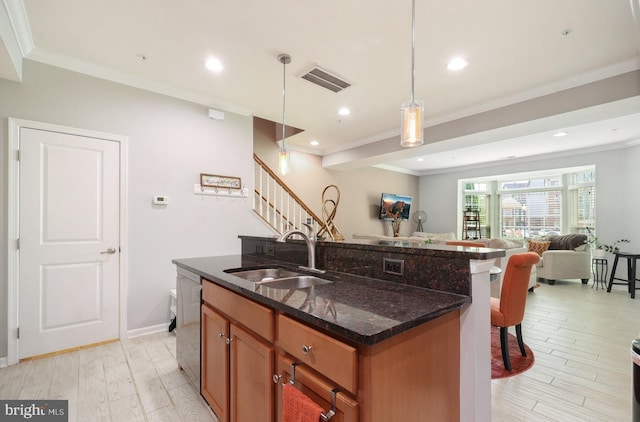 kitchen with brown cabinetry, a sink, visible vents, open floor plan, and a kitchen breakfast bar