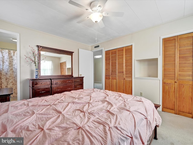 carpeted bedroom featuring ensuite bath, visible vents, two closets, and ceiling fan