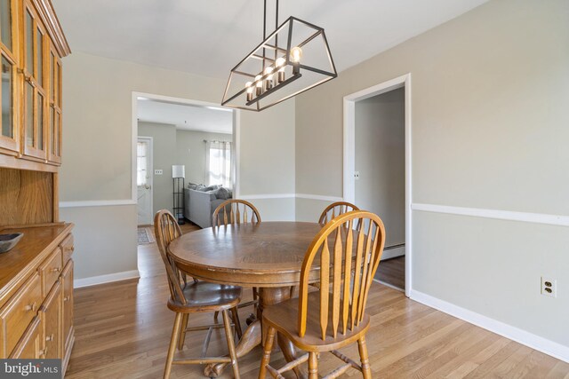 dining area with a baseboard heating unit, light wood-style flooring, and baseboards