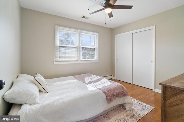 bedroom with wood finished floors, visible vents, baseboards, a closet, and baseboard heating