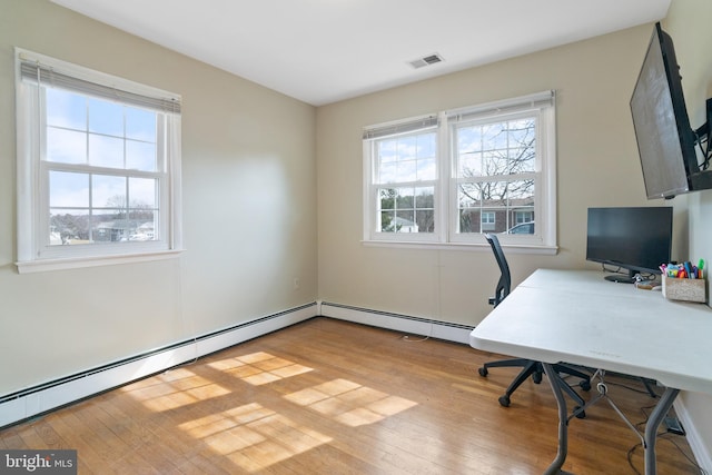 office space with baseboard heating, wood finished floors, visible vents, and a wealth of natural light