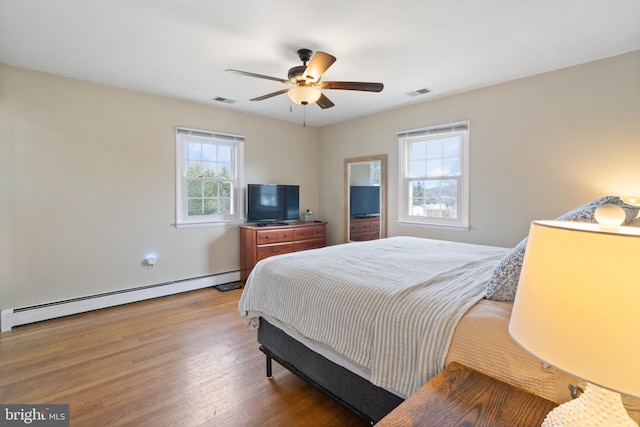 bedroom with baseboard heating, a ceiling fan, visible vents, and wood finished floors