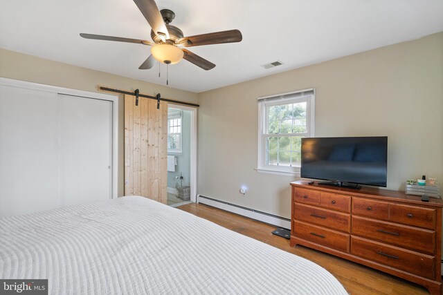 bedroom with visible vents, a barn door, baseboard heating, wood finished floors, and a closet