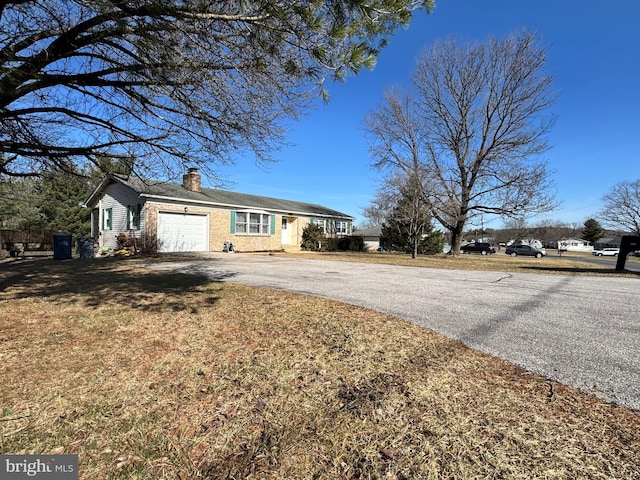 ranch-style home with a front yard, an attached garage, driveway, and a chimney