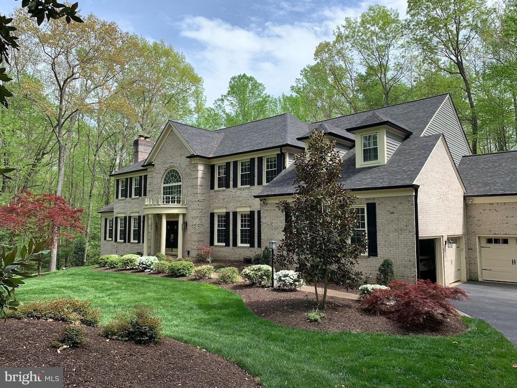 view of front of house featuring a front lawn, a chimney, brick siding, and aphalt driveway