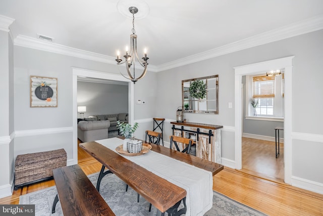 dining area featuring a notable chandelier, visible vents, crown molding, and light wood-style floors