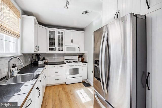 kitchen with decorative backsplash, white appliances, visible vents, and a sink