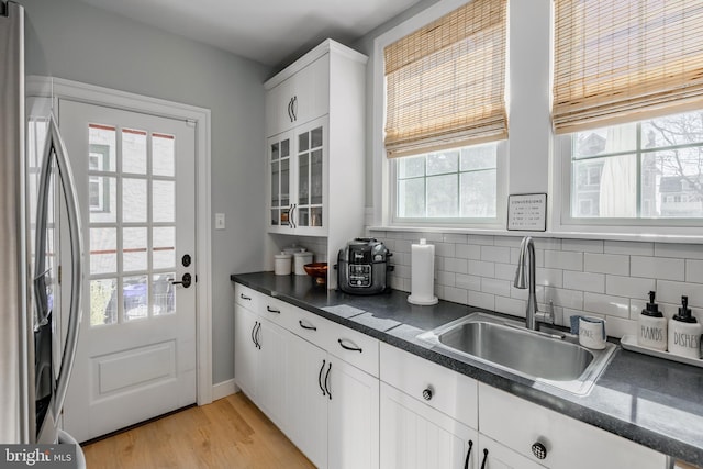 kitchen with a sink, backsplash, dark countertops, and stainless steel refrigerator with ice dispenser