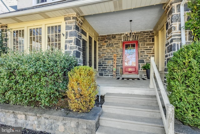 entrance to property with stucco siding, stone siding, and a porch